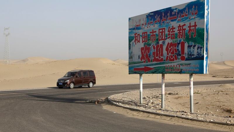 ARCHIVO - Un auto maneja por un desierto donde un cartel dice "Bienvenido al Nuevo Pueblo...
